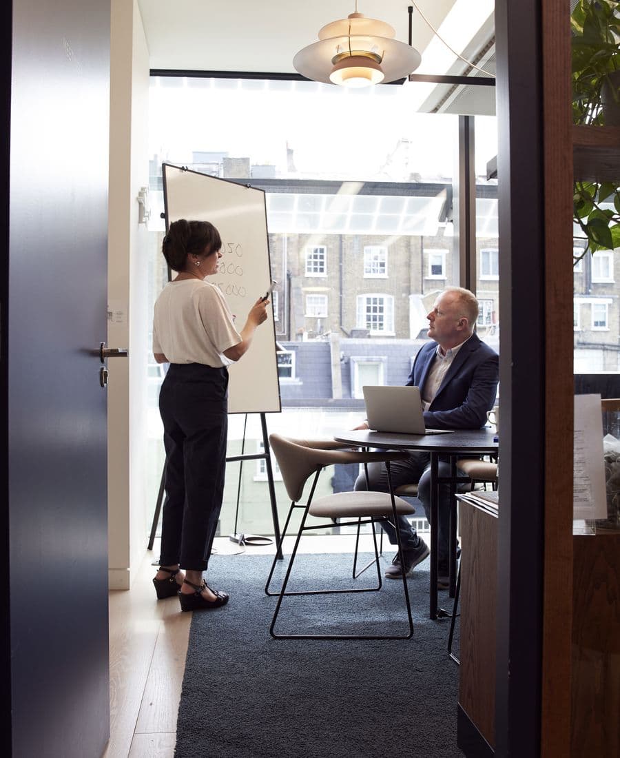 Deux personnes en séance de travail, l’une au paperboard, l’autre devant un ordinateur portable